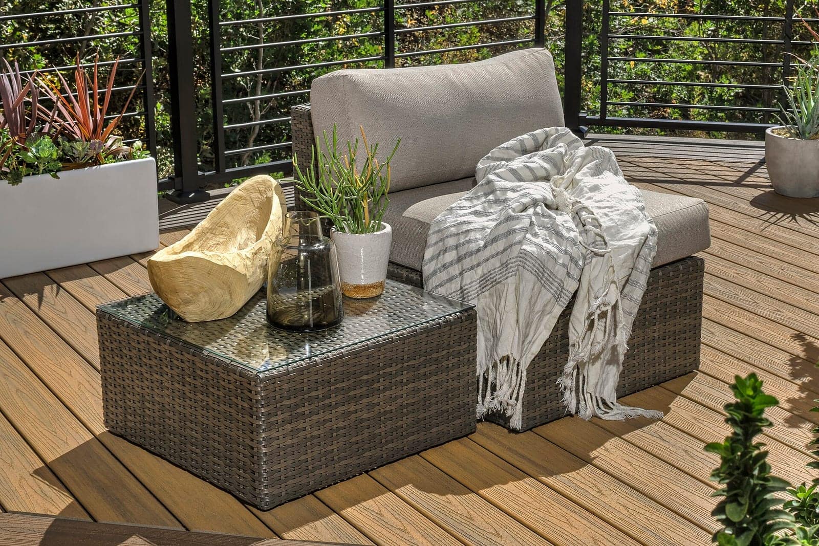 Finished residential deck with tan composite boards, black metal cable railing, and outdoor wicker furniture