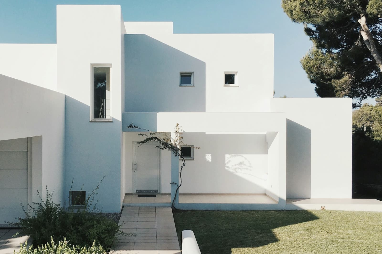 White stucco home exterior with clean wall planes, small windows, and a landscaped entry